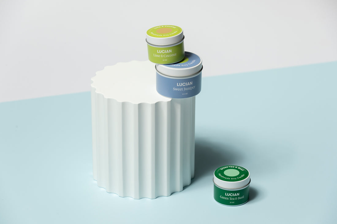 a mix of different scented green & blue hued soy wax travel tin candles on a white pillar in front of a blue backdrop