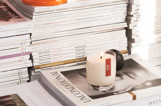 A lit Fireside glass candle on a stack of magazines